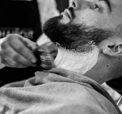grayscale photo of man shaving his beard